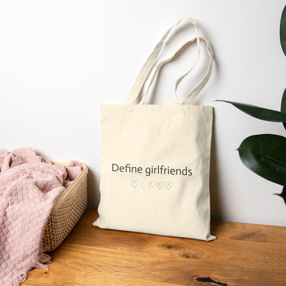 Natural canvas One Direction inspired tote bag featuring the “Define girlfriends” quote and pastel heart icons displayed on a wooden surface.
