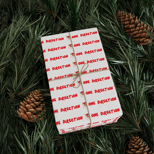 Pink fan-made One Direction inspired Christmas gift wrap featuring a repeating Santa Claus face pattern and red “One Direction” text, tied with twine and placed on pine branches with pinecones.